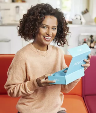 Woman smiling holding Spark Aligners package on the couch