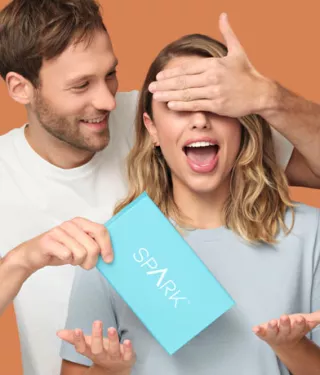 Man covering woman's eyes and holding Spark Aligners treatment box.