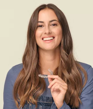 Woman wearing a blue shirt, holding aligners and smiling.