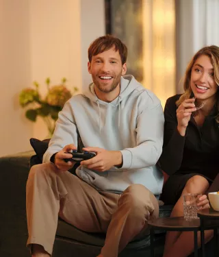 One man and one woman are playing video games, sitting in the living room. A third woman is taking off her Spark aligners.