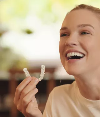 Close-up of a smiling young woman holding clear aligners that are being used to fix an overbite