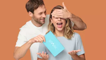 Man covering woman's eyes and holding Spark Aligners treatment box.