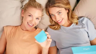 Two women smiling in bed holding Spark case and box. 