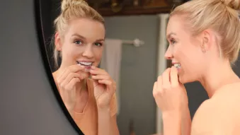 Woman smiling in front of a mirror putting Spark aligners on.