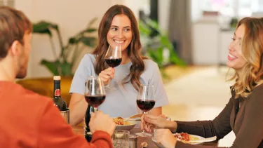Two woman and a man smiling having wine and dinner.