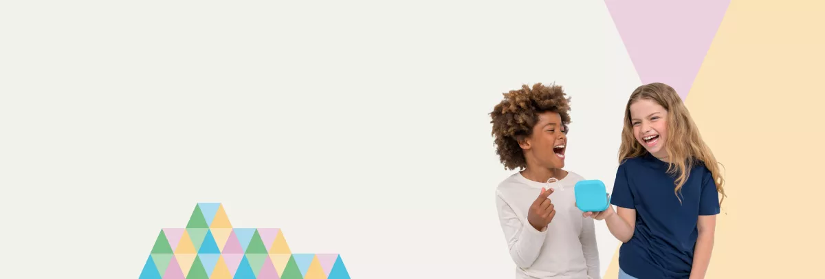 Smiling boy and girl holding Spark Junior clear aligners, showcasing the discreet and comfortable* orthodontic treatment for kids.